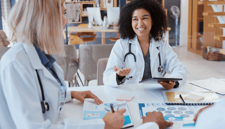 A young female doctor sitting at a table talking to other doctors.
