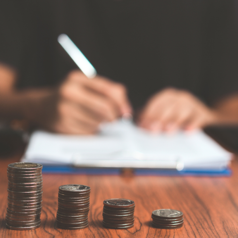 This is a person writing on paper with money in front of them.