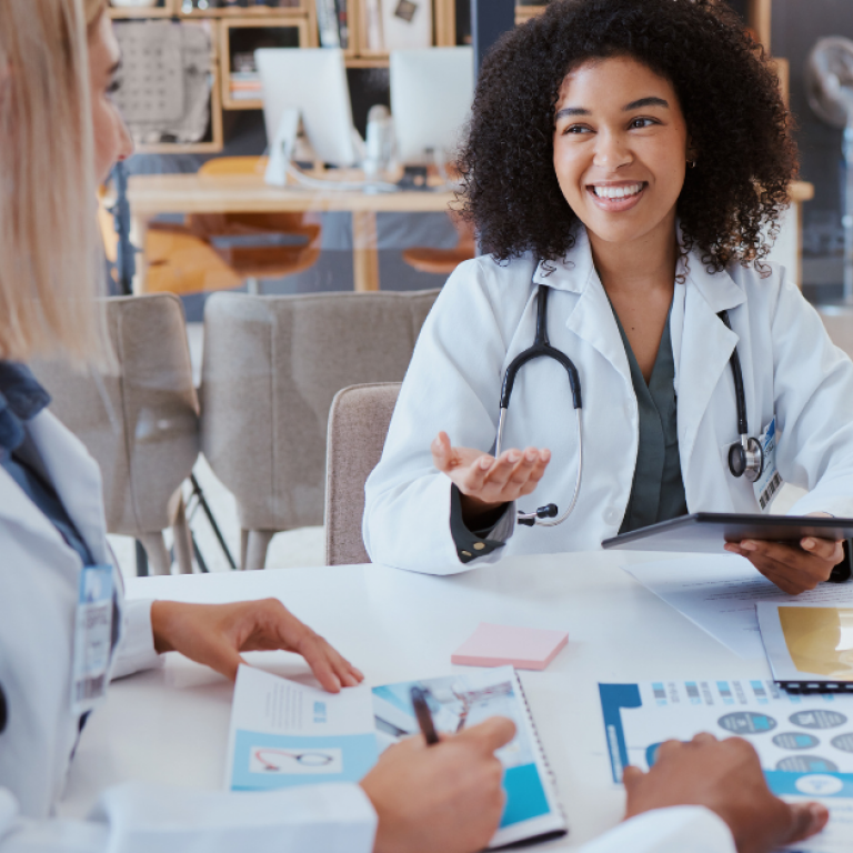 A young female doctor sitting at a table talking to other doctors.